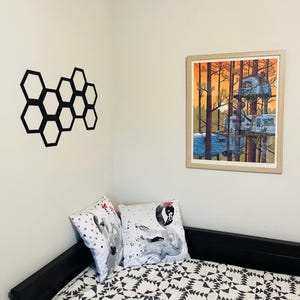 May include: A black and white honeycomb design on a white wall, a framed print of a treehouse with a camper van in the woods, and a black bed with a white and black patterned quilt and two pillows with a black and white bird design.