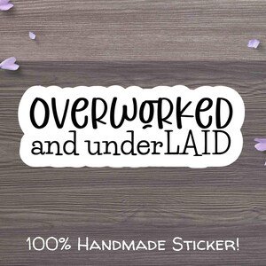 May include: White sticker with black text that reads "OVERWORKED and underLAID" on a wooden background. The text is in a playful, handwritten font. The sticker also includes the text "100% HANDMADE STICKER!"