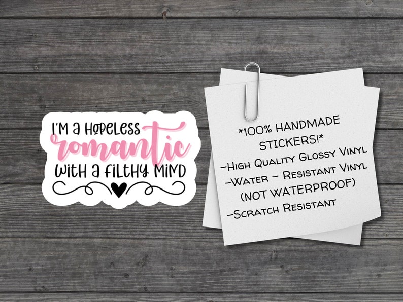 May include: A white sticker with a pink and black design. The sticker says "I'm a hopeless romantic with a filthy mind". The sticker is on a wooden background. The sticker is handmade and made of high quality glossy vinyl. It is water and scratch resistant, but not waterproof.