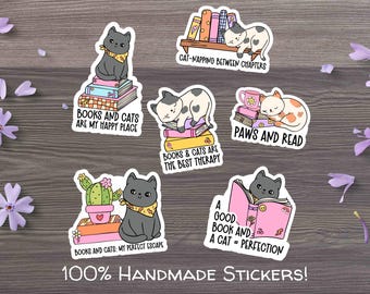 May include: A collection of handmade stickers featuring cats and books. Each sticker has a different design, including cats napping on books, reading, and with cacti. Text includes phrases like "Books and Cats are my happy place."