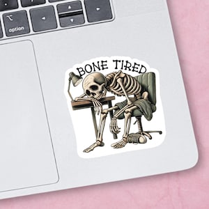 May include: A sticker featuring a cartoon skeleton sitting at a desk with a lamp, looking tired. The text "BONE TIRED" is above the skeleton.