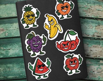 May include: A collection of colorful fruit stickers on a black surface. The stickers feature cartoon illustrations of a pineapple, banana, apple, cherries, grapes, watermelon, and orange, each with a defiant gesture and sunglasses.