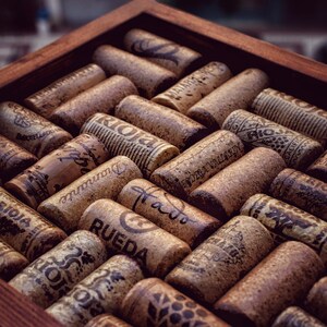 Puede incluir: Una caja de madera llena de diferentes tapones de vino. Los tapones son de corcho natural y tienen diferentes etiquetas y marcas, incluyendo "Rioja", "Rueda" y "Marqués de Murrieta".