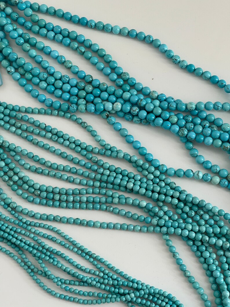 May include: A strand of turquoise blue beads, with multiple strands of beads layered on top of each other. The beads are round and smooth.