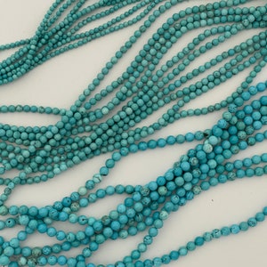 May include: A strand of turquoise beads, with a light blue color, arranged in a loose pile on a white surface.