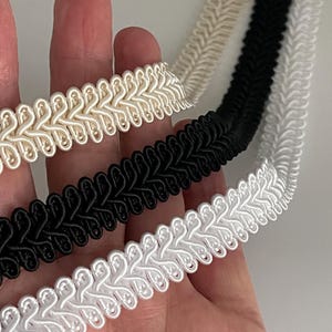 May include: Three different colors of braided trim, white, cream, and black. The trim is made of a soft, woven fabric and has a decorative, braided design.