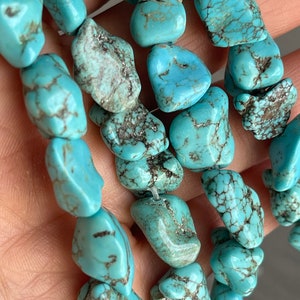 May include: A strand of turquoise gemstone beads. The beads are a light blue color with brown and black marbling. The beads are irregular in shape and have a smooth, polished finish.