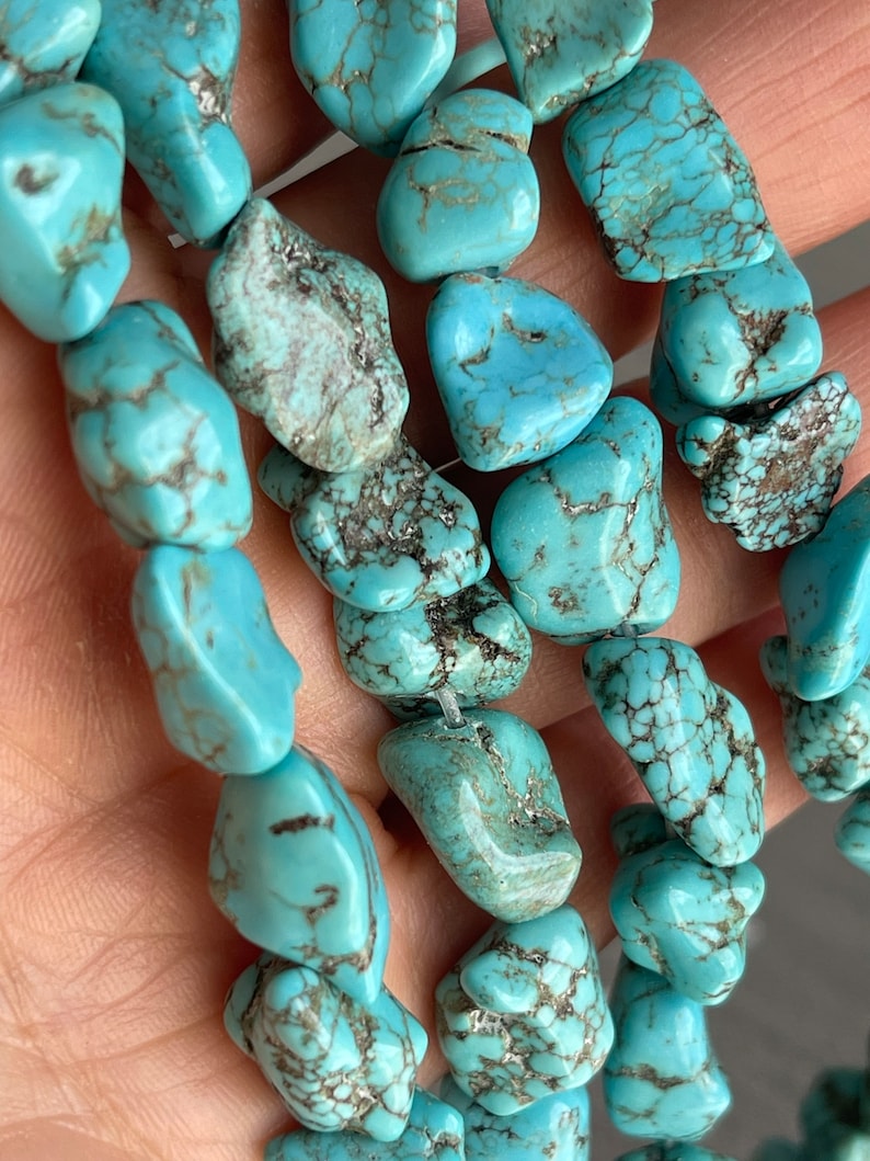May include: A strand of turquoise gemstone beads. The beads are a light blue color with brown and black marbling. The beads are irregular in shape and have a smooth, polished finish.