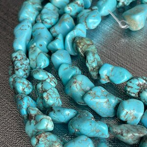 May include: A strand of turquoise gemstone beads, featuring a variety of shapes and sizes. The beads are a light blue color with brown veining and a smooth, polished finish.