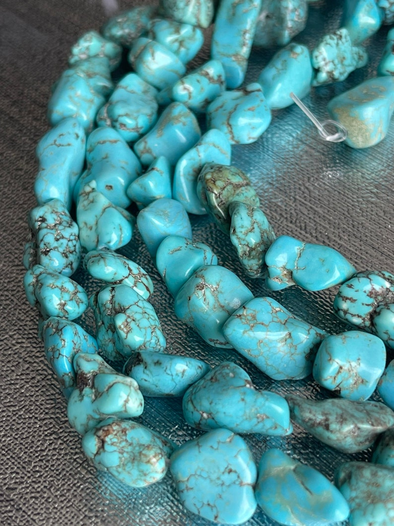 May include: A strand of turquoise gemstone beads, featuring a variety of shapes and sizes. The beads are a light blue color with brown veining and a smooth, polished finish.