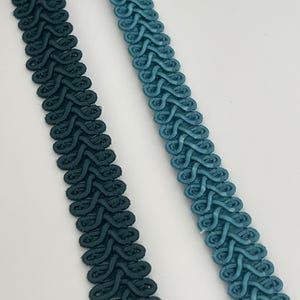 May include: Two strips of decorative gimp braid trim arranged vertically. One strip is a deep dark teal, and the other is a lighter, vibrant teal. Both feature a continuous, intricate woven loop pattern along the entire length.