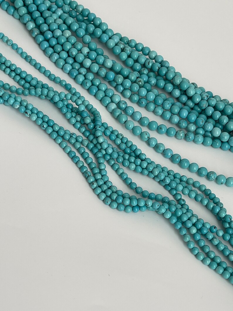 May include: A strand of turquoise beads, with multiple strands of beads layered on top of each other. The beads are a light blue color and have a smooth, round shape.