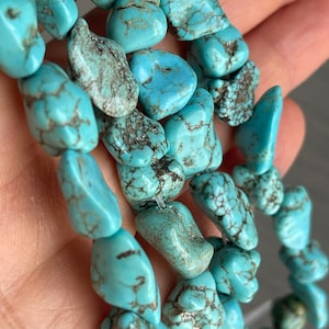 May include: A strand of turquoise gemstone beads, each bead is a unique, irregular shape with a light blue color and dark brown veining.