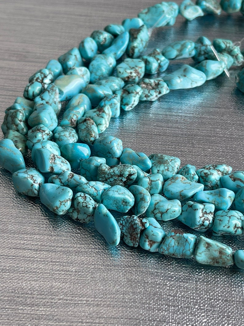May include: A strand of turquoise gemstone beads, featuring a mix of irregular shapes and sizes. The beads are a light blue color with brown veining and a matte finish.