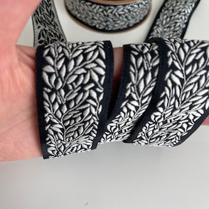 May include: Black and white ribbon with a silver leaf pattern. The ribbon is woven and has a textured surface.