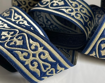 May include: Blue and cream trim ribbon with an intricate, repeating pattern. The ribbon is woven with a raised texture and has a subtle sheen.