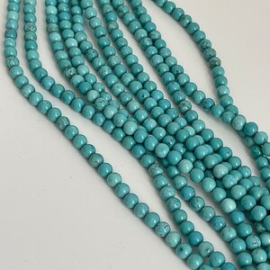 May include: A strand of turquoise beads, with multiple strands of the beads laid out in a row. The beads are a light blue color and have a smooth, round shape.