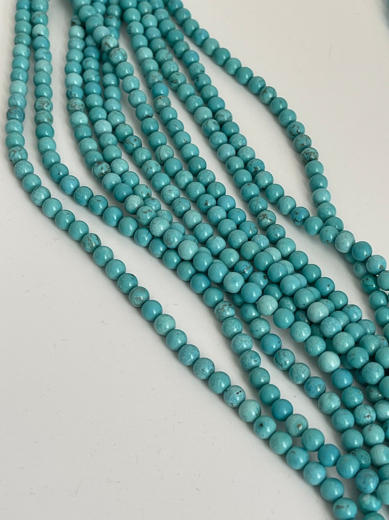 May include: A strand of turquoise beads, with multiple strands of the beads laid out in a row. The beads are a light blue color and have a smooth, round shape.