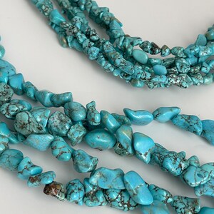 May include: A multi-strand turquoise necklace made of irregular, chip-shaped beads. The necklace is made of several strands of turquoise beads, each strand is about 1/4 inch wide. The beads are a light blue color with brown and black marbling.
