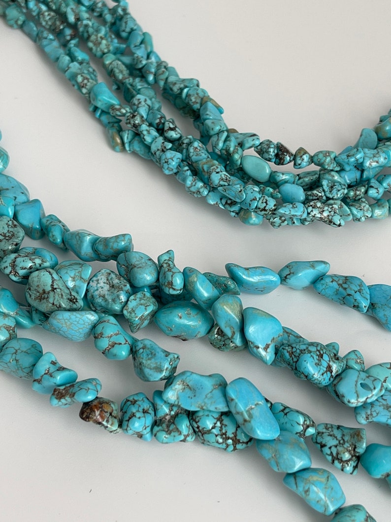 May include: A multi-strand turquoise necklace made of irregular, chip-shaped beads. The necklace is made of several strands of turquoise beads, each strand is about 1/4 inch wide. The beads are a light blue color with brown and black marbling.