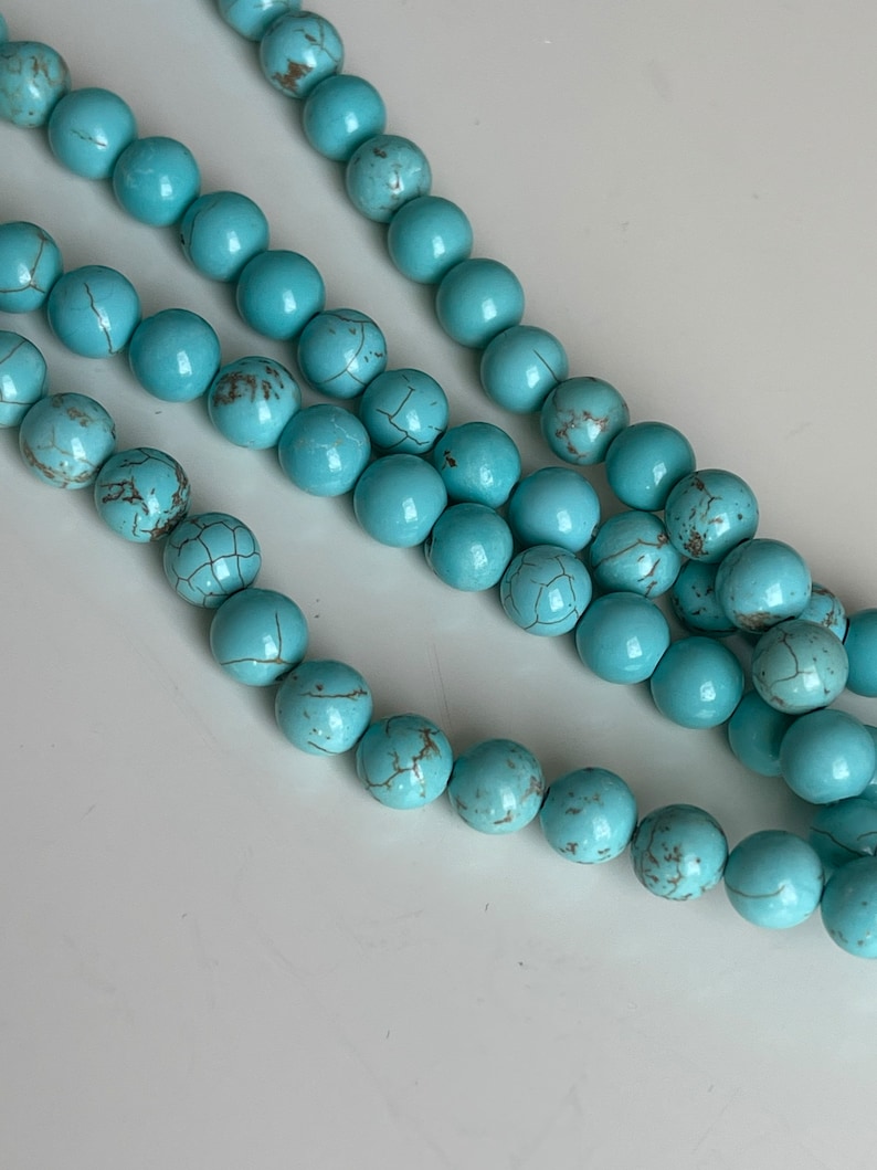 May include: A strand of turquoise blue beads with brown marbling. The beads are round and smooth.