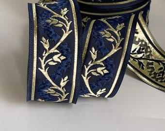 May include: A roll of navy blue ribbon with a gold floral design. The ribbon features a repeating pattern of stylized flowers and leaves, with gold trim along the edges. The ribbon is likely used for crafting or decorative purposes.