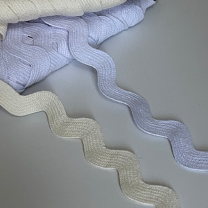 May include: Two white cotton zig zag trim, one is a lighter shade of white than the other. The trim is folded and stacked on top of each other.
