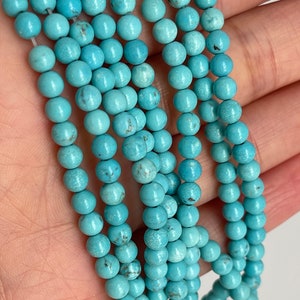 May include: A strand of turquoise beads, each bead is round and smooth with a light blue color. The beads are strung on a clear thread and are arranged in a loose pile.