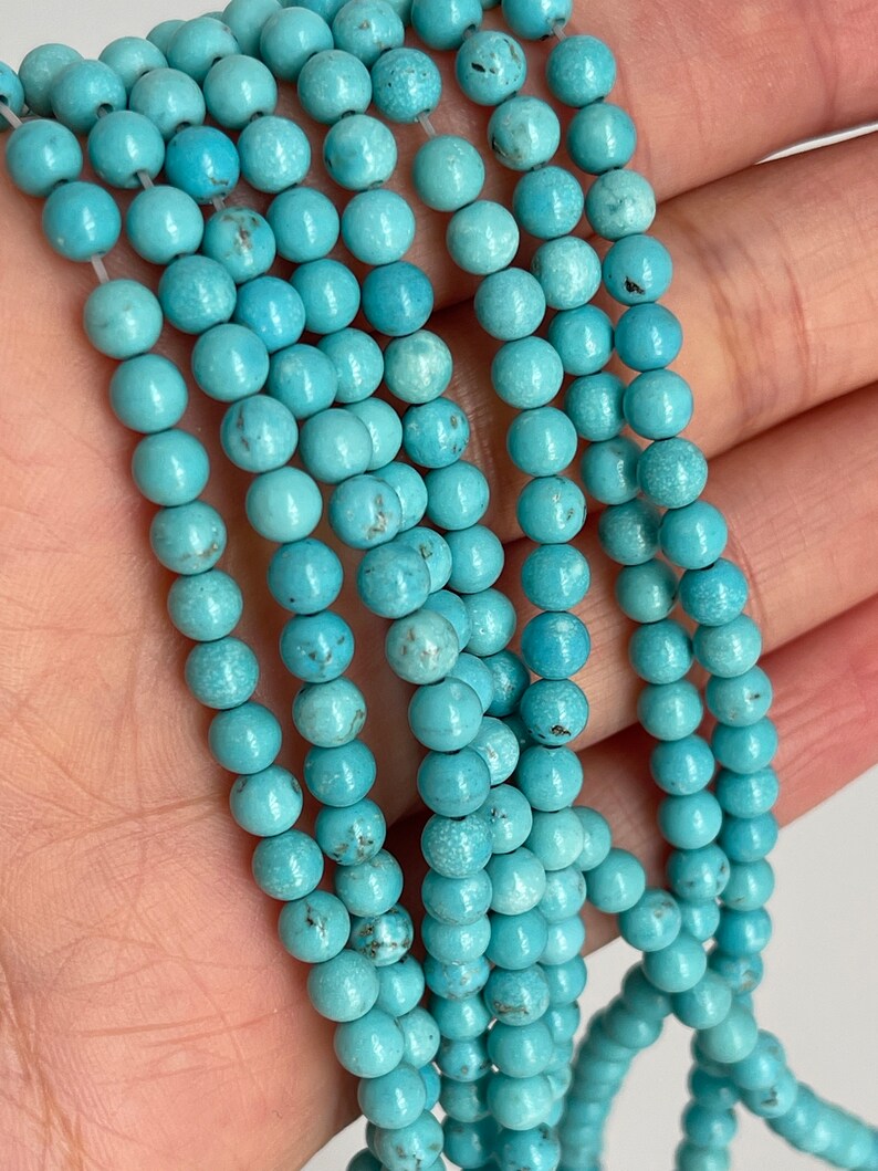 May include: A strand of turquoise beads, each bead is round and smooth with a light blue color. The beads are strung on a clear thread and are arranged in a loose pile.