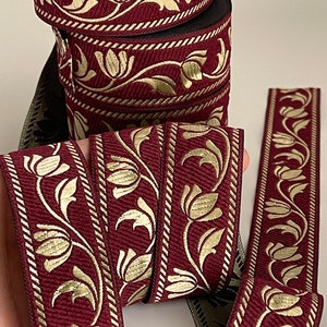Peut inclure: Galon de couleur bordeaux et or avec un motif floral. Le galon est tissé avec un design texturé et présente un motif répétitif de tulipes et de feuilles stylisées.