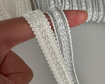May include: Two white beaded trims with a silver thread running through one of the trims. The trims are made of white beads and a white fabric base.