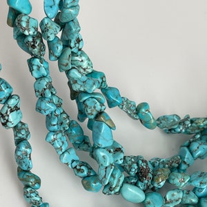 May include: A strand of turquoise gemstone beads, featuring a mix of irregular shapes and sizes. The beads are a vibrant blue-green color with black veining throughout.