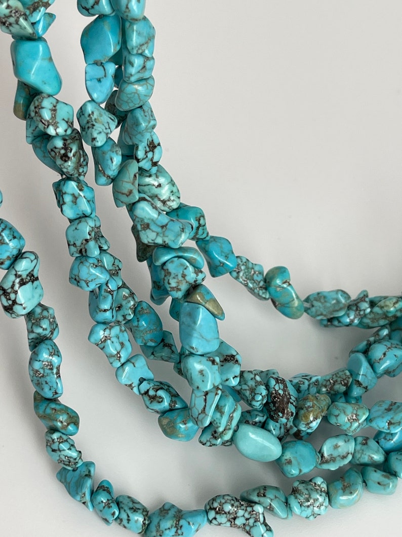 May include: A strand of turquoise gemstone beads, featuring a mix of irregular shapes and sizes. The beads are a vibrant blue-green color with black veining throughout.