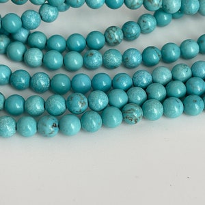 May include: A strand of turquoise blue beads, each bead is round and has a slightly rough texture.