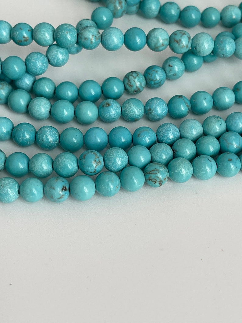 May include: A strand of turquoise blue beads, each bead is round and has a slightly rough texture.
