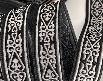 May include: Black and white decorative ribbon with an ornate, repeating pattern. The ribbon is tightly coiled, showcasing the detailed design and texture. The pattern features stylized floral and geometric elements, creating a classic, elegant look. Ideal for crafting and embellishments.