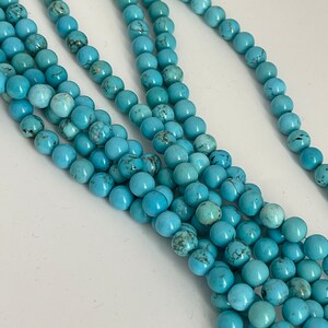 May include: A strand of turquoise beads, featuring a light blue color with dark blue veining. The beads are round and smooth, and they are strung together on a clear thread.
