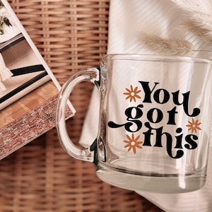 May include: A clear glass mug with a black and orange design that says "You got this".