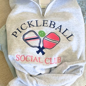 May include: Gray sweatshirt with a navy blue embroidered design that says "Pickleball Social Club" with two crossed pickleball paddles and a green ball.