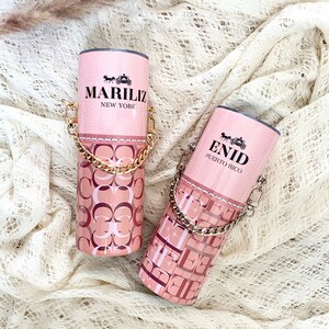 May include: Two pink and gold tumblers with a chain handle. The tumblers have a pink and white pattern with the text "MARILIZ NEW YORK" and "ENID PUERTO RICO".