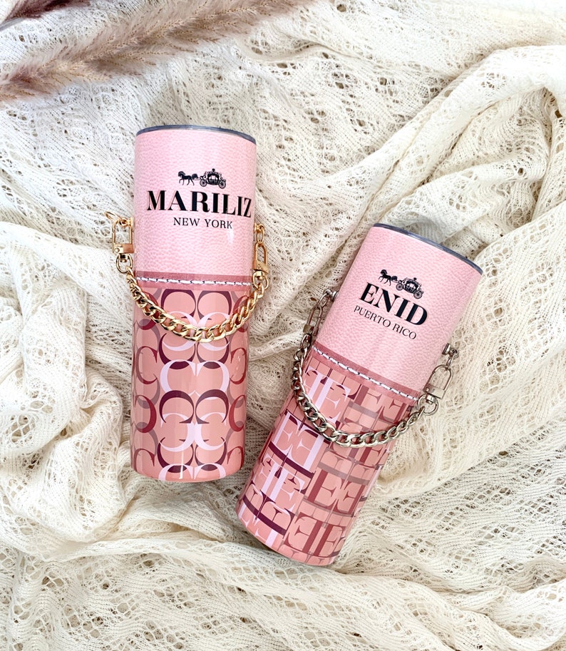 May include: Two pink and gold tumblers with a chain handle. The tumblers have a pink and white pattern with the text "MARILIZ NEW YORK" and "ENID PUERTO RICO".
