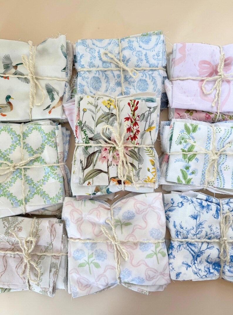 Puede incluir: Paquetes de cuadrados de tela atados con hilo, con varios patrones florales y de naturaleza. Los dise&ntilde;os incluyen patos, flores, lazos e impresiones florales azules. Las telas son en tonos de blanco, azul, rosa y verde.