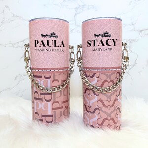 May include: Two pink stainless steel tumblers with a silver chain handle. The tumblers have a pink and white patterned design with the names "Paula" and "Stacy" on the front. The text "Washington, DC" is below "Paula" and "Maryland" is below "Stacy".
