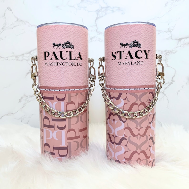 May include: Two pink stainless steel tumblers with a silver chain handle. The tumblers have a pink and white patterned design with the names "Paula" and "Stacy" on the front. The text "Washington, DC" is below "Paula" and "Maryland" is below "Stacy".