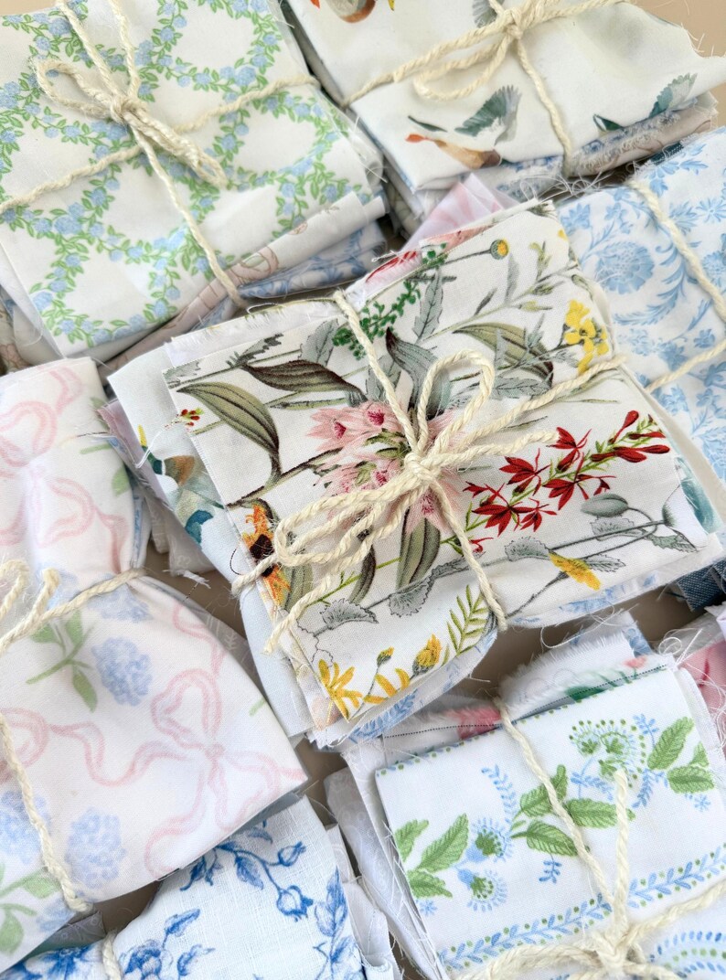 Puede incluir: Conjunto de paquetes de tela atados con hilo. La tela presenta varios patrones florales y bot&aacute;nicos en tonos azules, rosas, amarillos y verdes sobre un fondo blanco. Los paquetes est&aacute;n apilados.