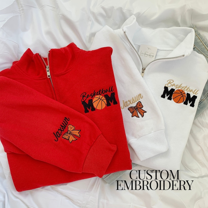 May include: Two sweatshirts with custom embroidery. One red sweatshirt with "Basketball Mom" and "Jaxsun" embroidered on it. One white sweatshirt with "Basketball Mom" embroidered on it.