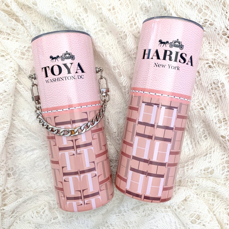 May include: Two pink and brown patterned stainless steel tumblers with a silver chain handle on one. The tumbler on the left says "TOYA WASHINGTON, DC" and the tumbler on the right says "HARISA New York".