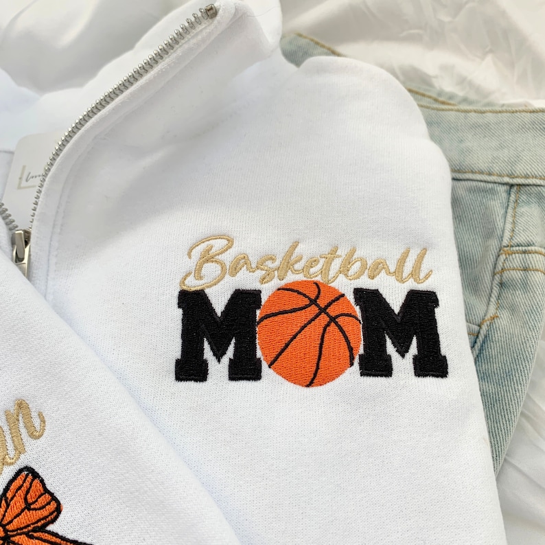 May include: White zippered sweatshirt with the text "Basketball Mom" embroidered in black and gold with an orange basketball graphic.