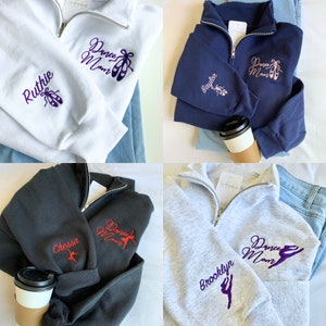 May include: Four sweatshirts in different colours, each with a zip and embroidered text. The text includes "Dance Mom" and a dancer silhouette. Each sweatshirt has a different name embroidered on the sleeve: Ruthie, Baylor, Chessa, and Brooklyn.