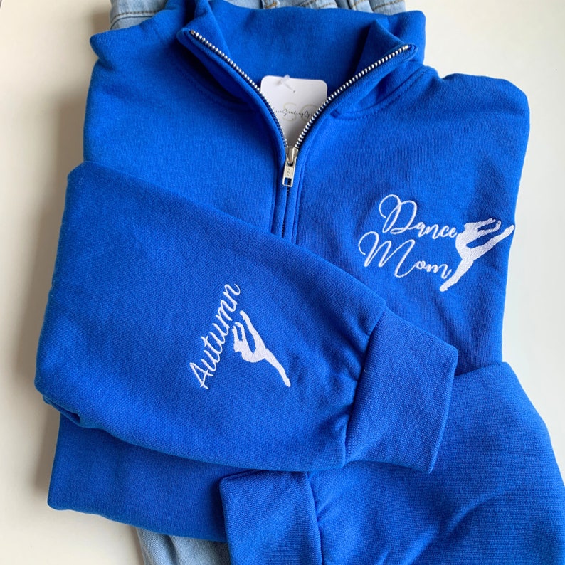 May include: Royal blue zip-up sweatshirt with white embroidery. The front reads "Dance Mom" with a stylised dancer. The left sleeve reads "Autumn" with a stylised dancer.